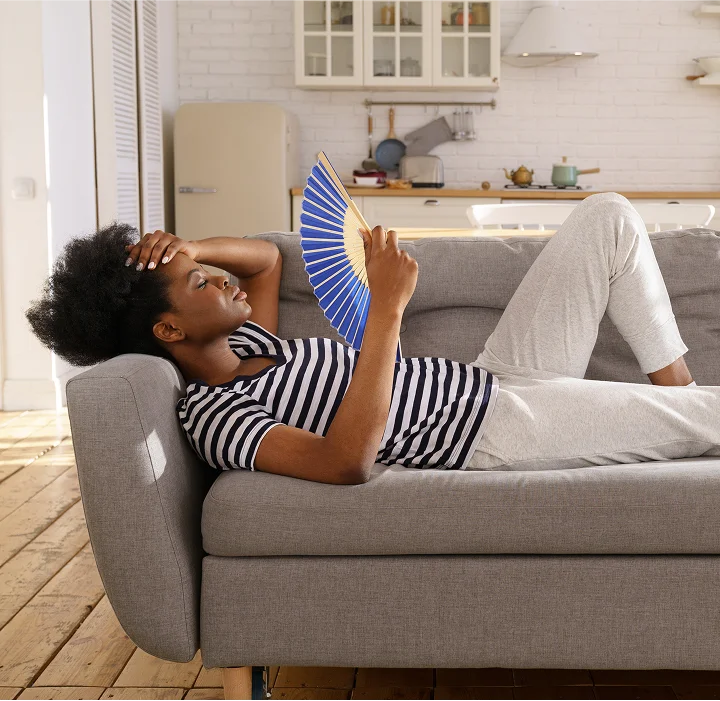 A woman fans herself while laying on a couch