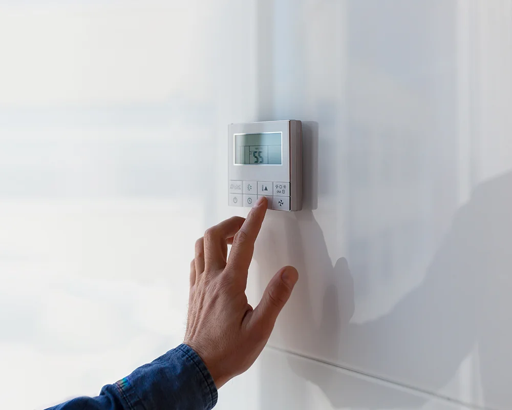 a hand adjusts the settings on a home thermostat